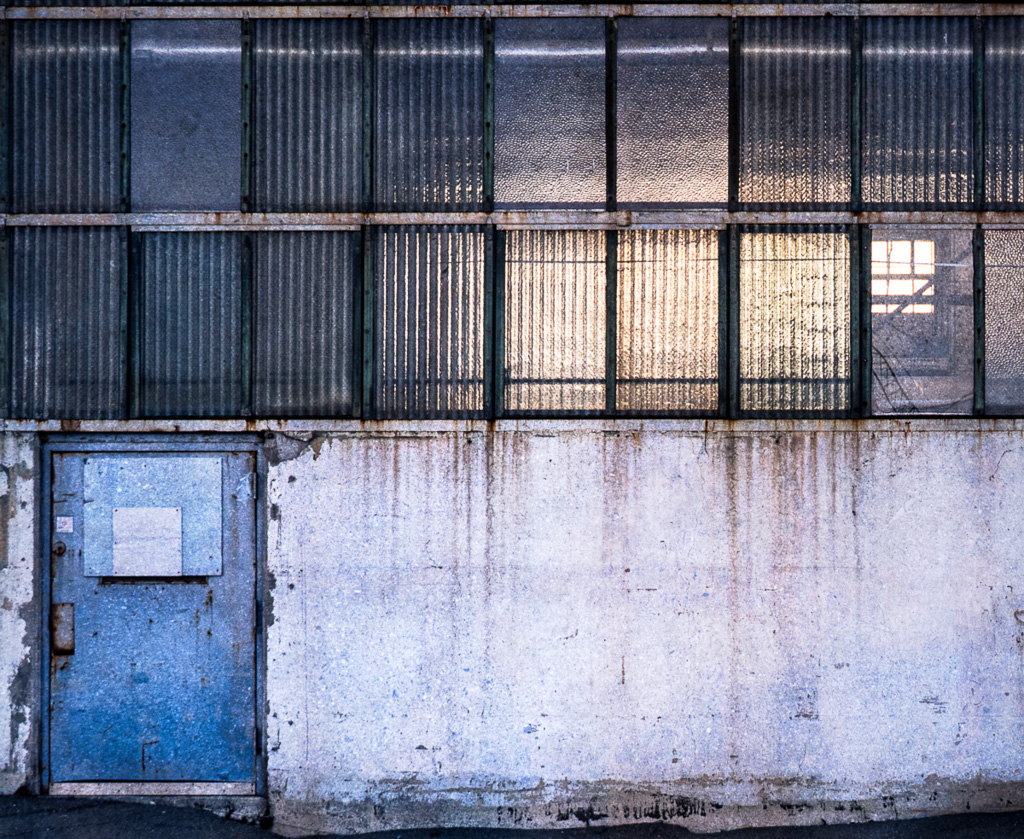 Soft light filters through corrugated windows above a rust-stained wall. The absence of workers is palpable.